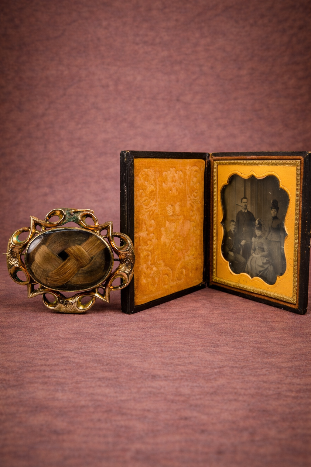 Victorian gold-plated mourning brooch with woven hair displayed beside an open Civil War–era ambrotype family portrait in its original leather case against a warm brown studio background.