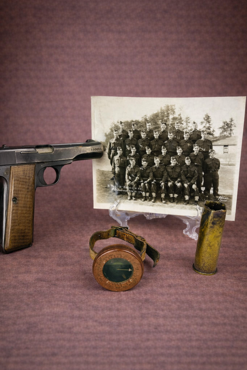 Belgian Browning FN Model 1922 WWII-era pistol displayed alongside a Canadian WWII artillery group photograph, paratrooper compass, and shell casing against a warm brown studio background.