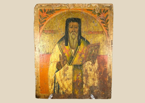 Antique 18th-century Russian Orthodox icon, hand-painted in tempera with gold leaf, depicting a saint in blessing pose with Gospel book, Cyrillic inscription, and floral motifs. Provincial workshop devotional panel with historic patina.