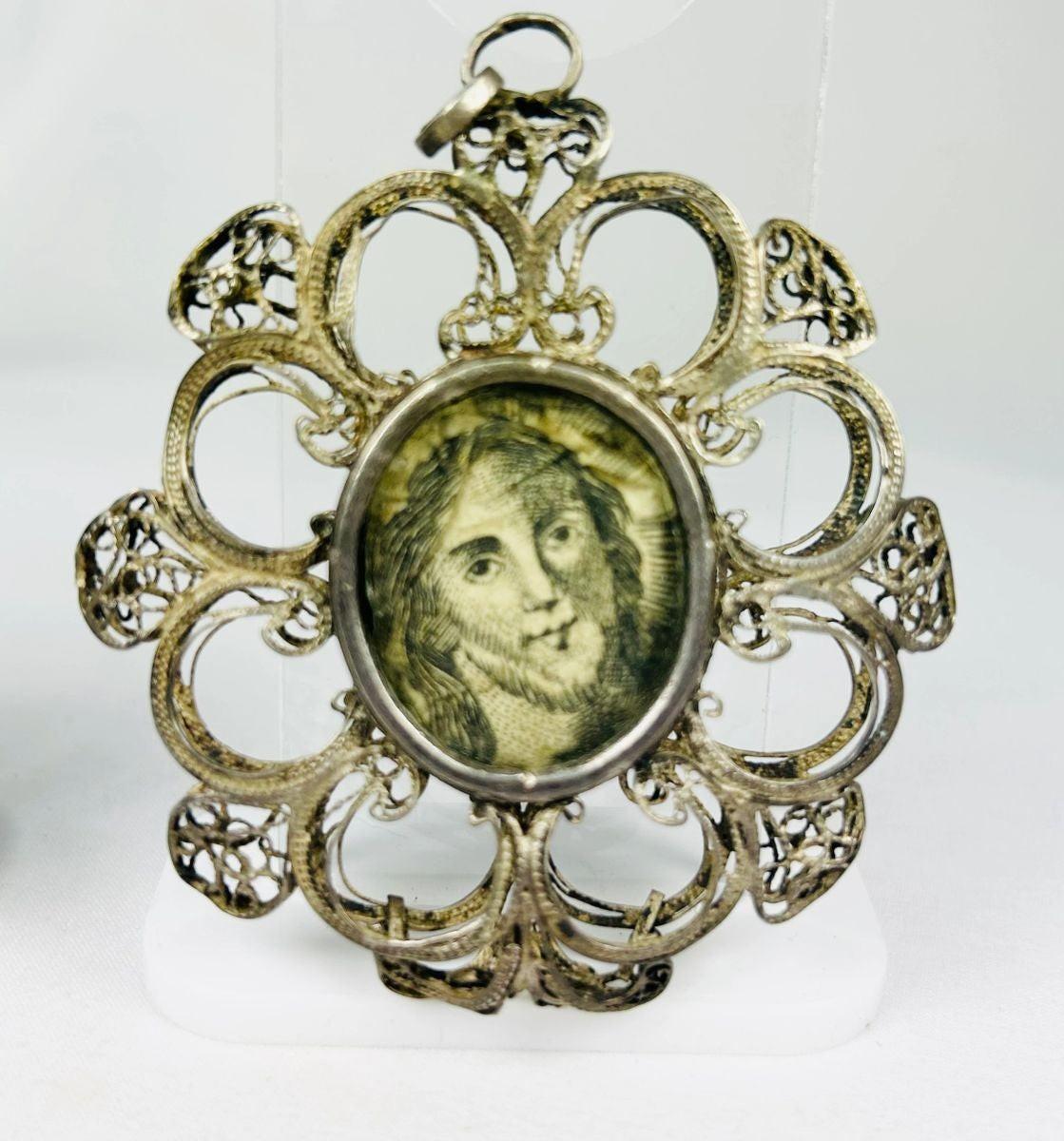 Antique 19th-century Catholic devotional pendant with ornate silver filigree frame and engraved portrait of Christ under glass, likely Italian or Spanish origin.