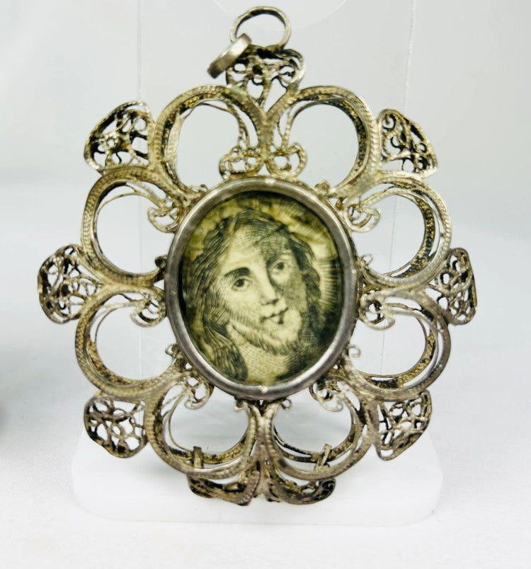 Antique 19th-century Catholic devotional pendant with ornate silver filigree frame and engraved portrait of Christ under glass, likely Italian or Spanish origin.