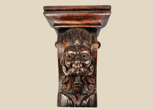 Antique 19th-century European wooden corbel, hand-carved with a grotesque crowned face featuring a prominent mustache and ornamental details. Dark natural patina, Gothic-inspired design, and architectural functionality. Serves as both structural support and decorative element, reflecting historic woodcarving traditions and Gothic revival aesthetics.