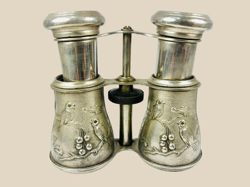 Antique 19th century opera glasses with silver-plated body, finely engraved bird and floral motifs, and adjustable mechanism. Elegant collectible binoculars used for theater and opera viewing, with rich patina and decorative craftsmanship.