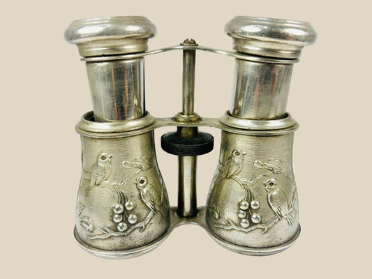 Antique 19th century opera glasses with silver-plated body, finely engraved bird and floral motifs, and adjustable mechanism. Elegant collectible binoculars used for theater and opera viewing, with rich patina and decorative craftsmanship.