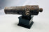 Side view of an excavated 18th-century British signal cannon displayed on a black museum stand.