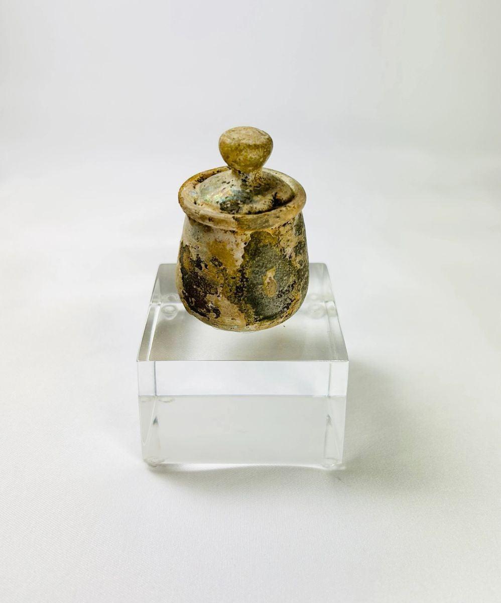 Roman–Parthian era glass ointment jar displaying natural iridescence and original knobbed lid.