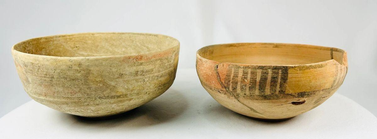 Two ancient Indus Valley terracotta bowls, circa 2nd–3rd millennium BCE; one plain with natural earthen patina, the other decorated with geometric polychrome painted motifs, both exhibiting age wear and archaeological restoration.