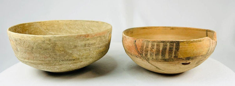 Two ancient Indus Valley terracotta bowls, circa 2nd–3rd millennium BCE; one plain with natural earthen patina, the other decorated with geometric polychrome painted motifs, both exhibiting age wear and archaeological restoration.