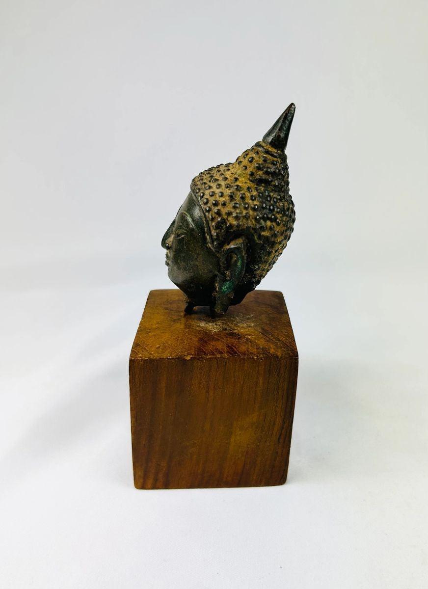 Ancient Asian bronze Buddha head from Thailand featuring half-closed eyes and gentle smile