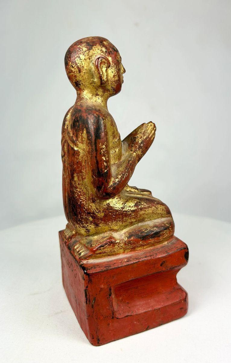 Three-quarter angle of Southeast Asian monk statue, emphasizing posture, robe folds, and lacquer inscriptions.