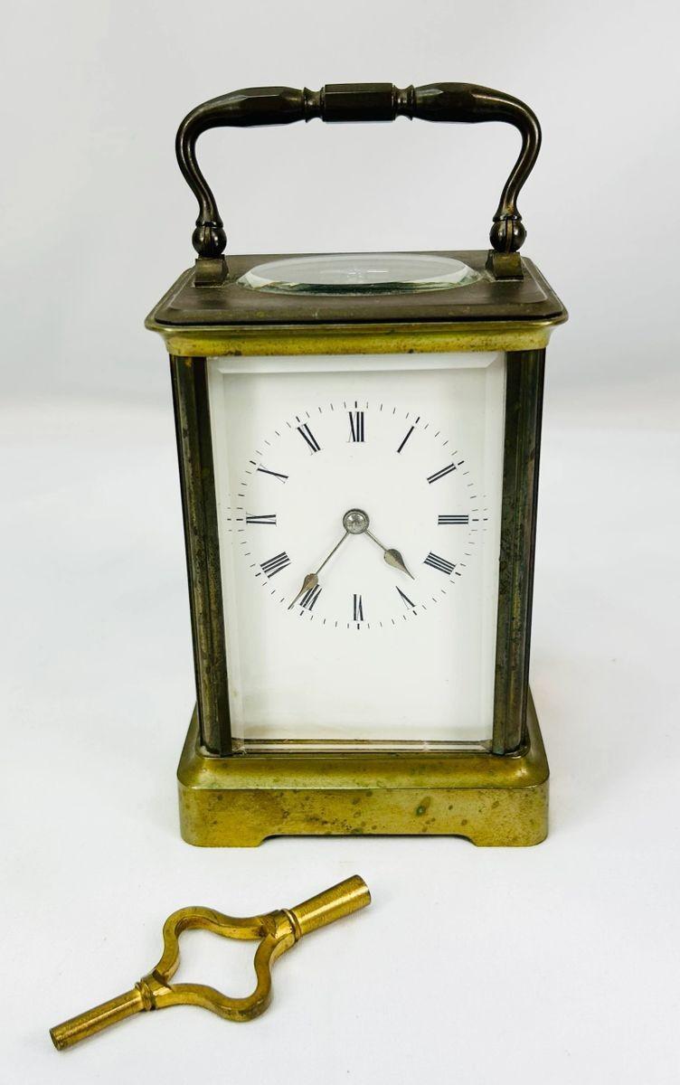 Front view of antique French carriage clock with white enamel dial and visible escapement.