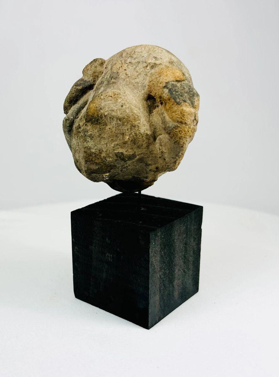 Ancient carved stone mask fragment mounted on black wooden stand