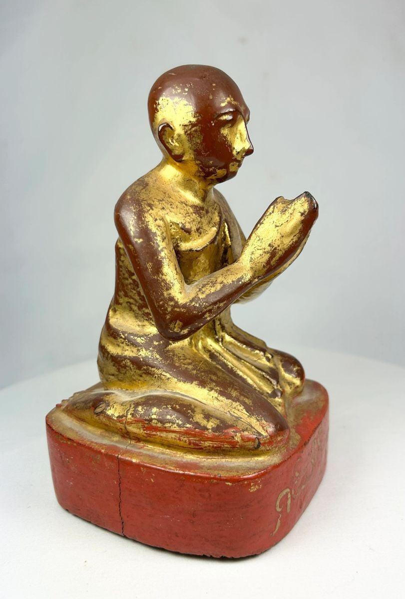 Angled view of Burmese monk statue emphasizing prayerful pose and intact gold leaf remnants.