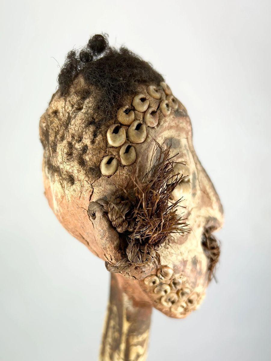 Sepik River ceremonial dagger with carved ancestral head, cowrie shell inlays, and human hair, left-angled view showcasing facial details and tribal motifs.