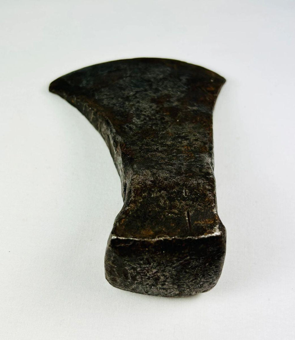 Close-up photo of antique forged iron axe head with visible blacksmith hammer marks and weathered surface.