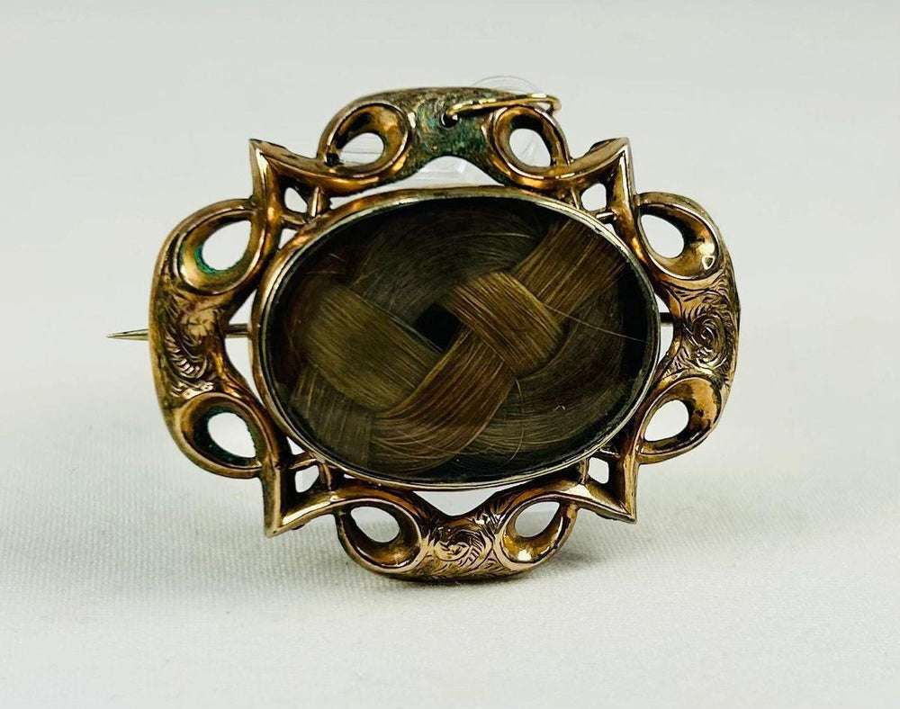 Museum-style photograph of a mid-19th-century Victorian mourning hairwork brooch.