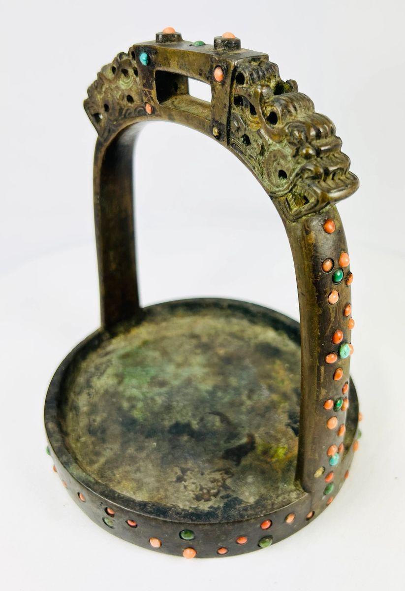 Detail shot showing textured bronze surface and colorful inlay on Mongolian saddle stirrup.