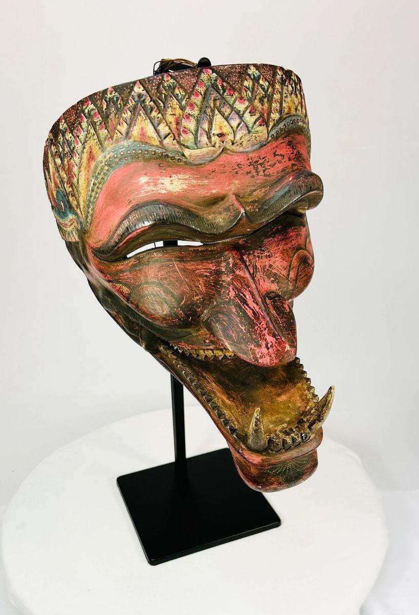 Angled view of a late 19th-century Javanese carved wooden Cakil mask with polychrome paint on a black display stand.