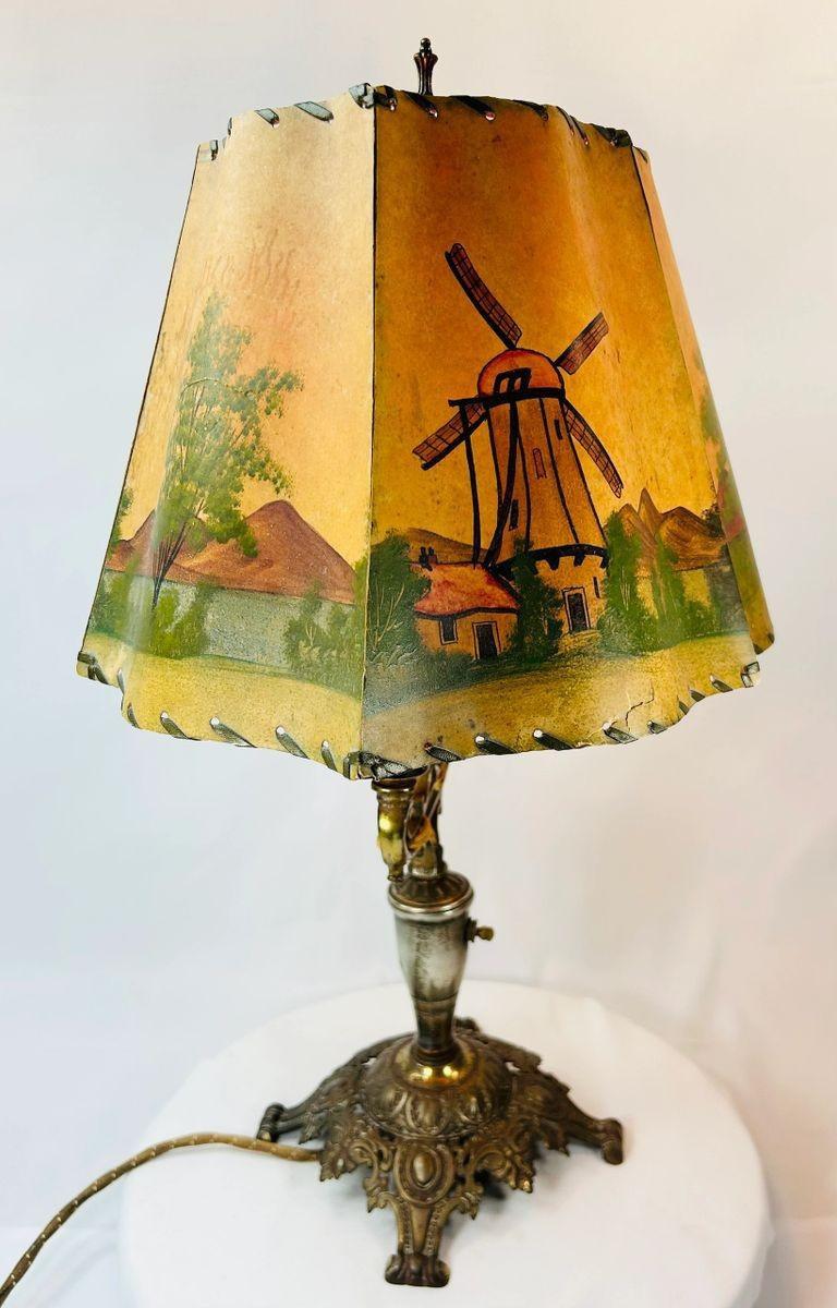 Early 20th century decorative lighting piece with ornate metal armature and scenic shade