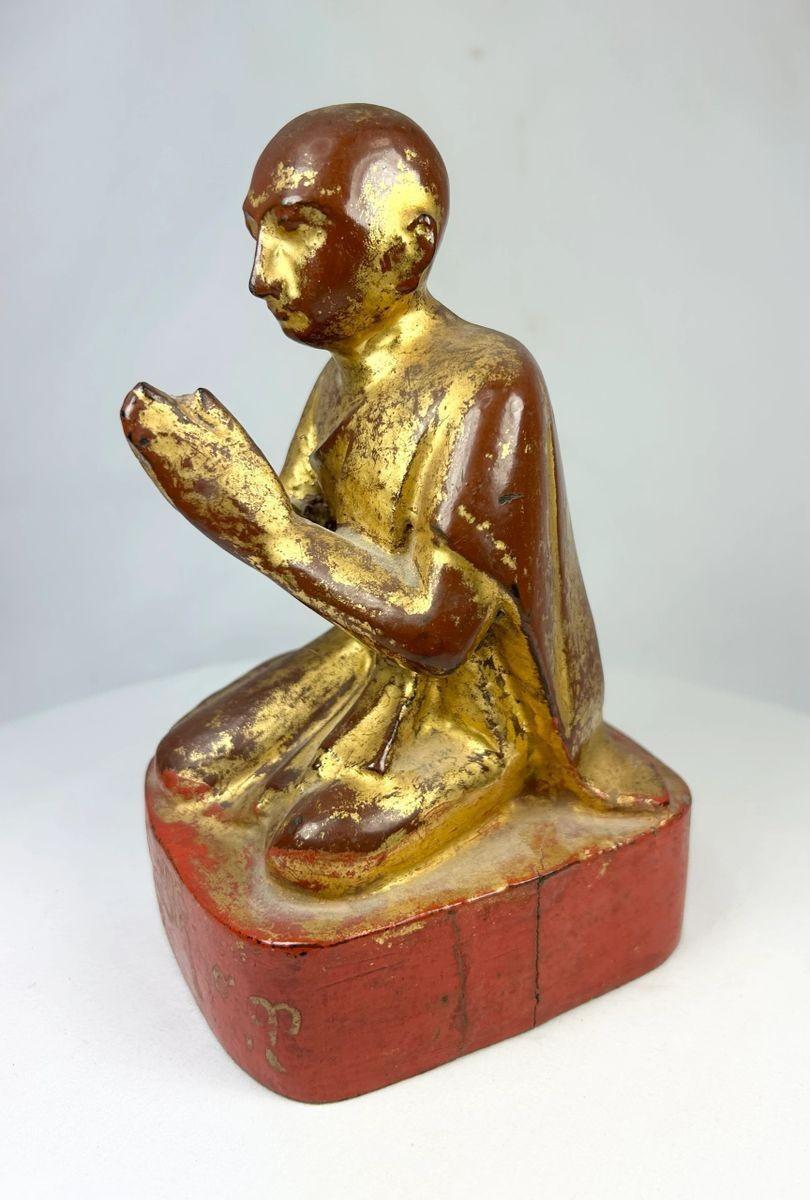 Side profile of antique Burmese Buddhist monk sculpture showing carved robe details and gilded surface.