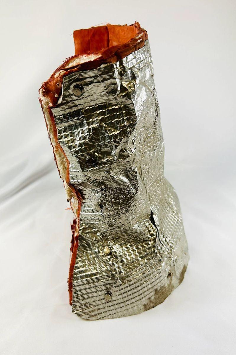 Authentic flown NASA Space Shuttle insulation blanket made of fibrous silica batting with reflective silver thermal surface and orange edge seal, used in the Orbiter Thermal Protection System (TPS), stamped April 1983 with serial number and manufacturer code visible on the metal tag, approximately 11 by 10 inches, aerospace artifact from the Space Shuttle Program.