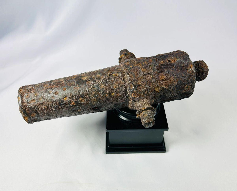 Angled overhead view of an 18th-century British signal cannon with heavy rust encrustation on a black museum display stand.