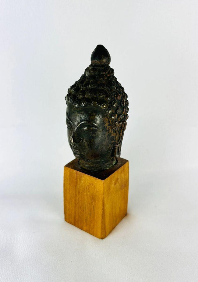 Historical bronze Buddha head on wooden base reflecting meditation iconography