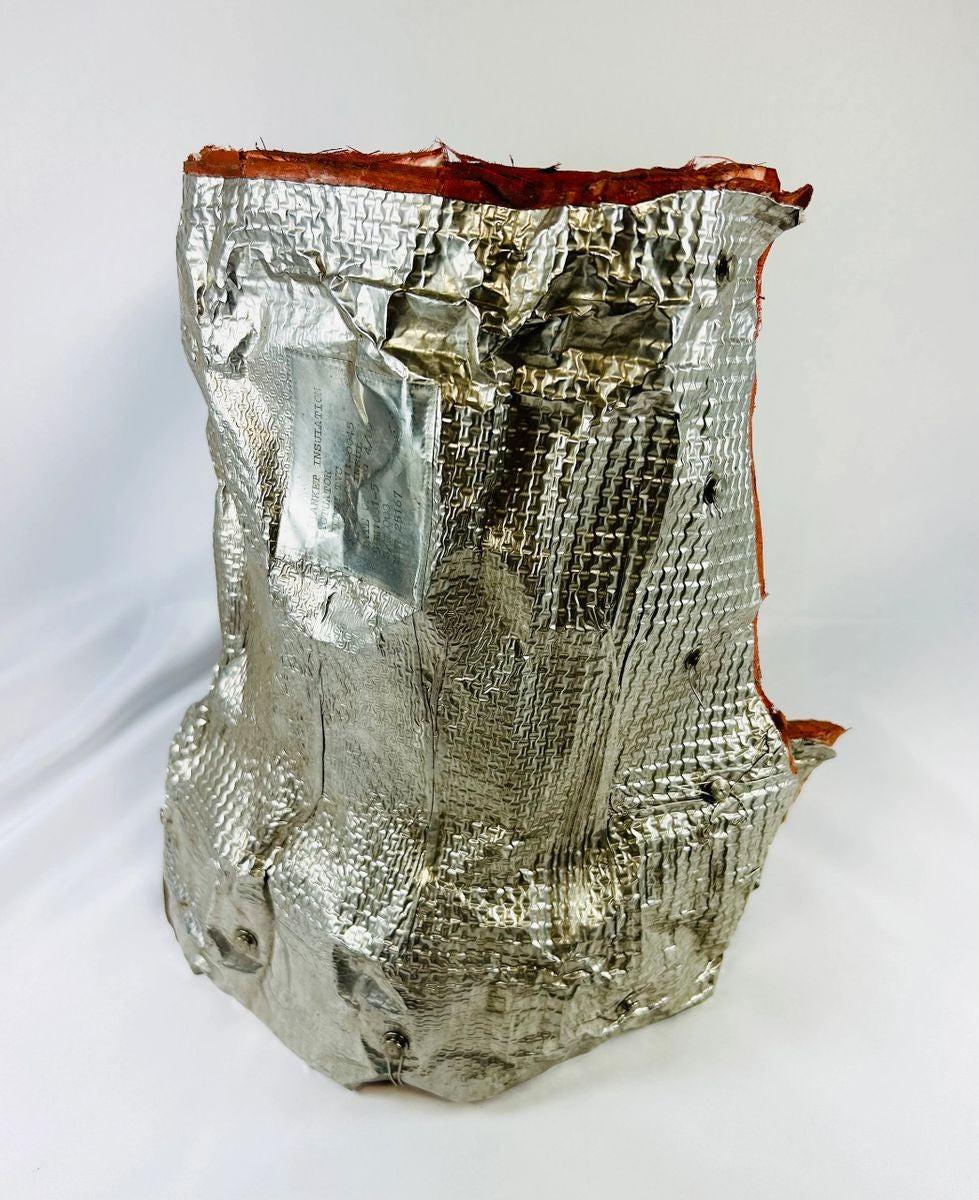 Authentic flown NASA Space Shuttle blanket insulation, made of fibrous silica batting with reflective metallic surface and orange edge trim. Stamped April 1983 with manufacturer code and serial number, used in the orbiter’s Thermal Protection System for pitch actuator thermal shielding.