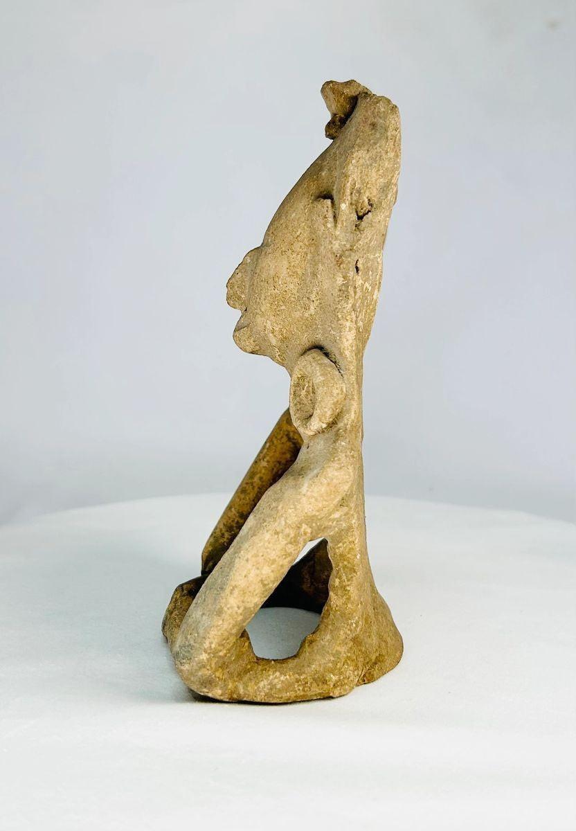 Ancient Mesoamerican ceramic figurine showing a stylized seated human form with rounded facial features and ritual headpiece, likely Zapotec or Olmec influence