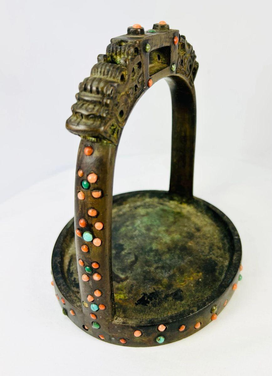 Museum-style presentation of Tibetan stirrup with mythical dragon motifs and gemstone inlay.