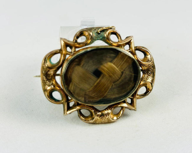 Victorian mourning hairwork brooch with braided human hair beneath beveled glass, mid-19th century.