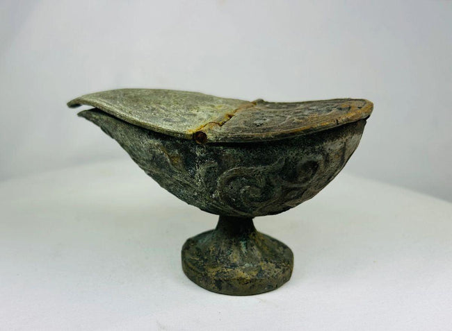 Han Dynasty bronze oil lamp on flared pedestal base, showing curved spout and engraved swirling patterns with aged green patina.