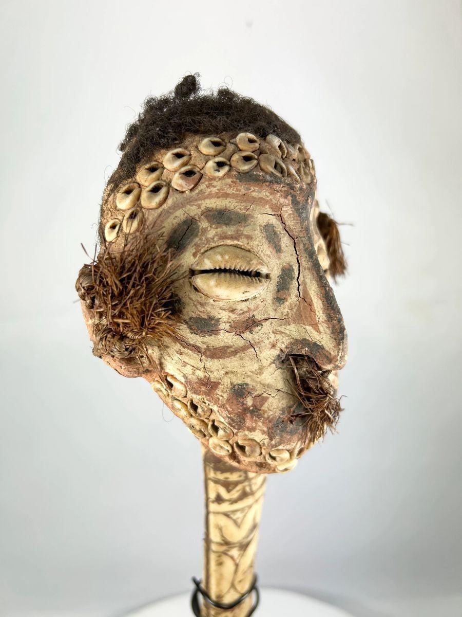Front view of 19th-century Papua New Guinea bone dagger featuring anthropomorphic carved head, cowrie shells, and ritual hair adornment.