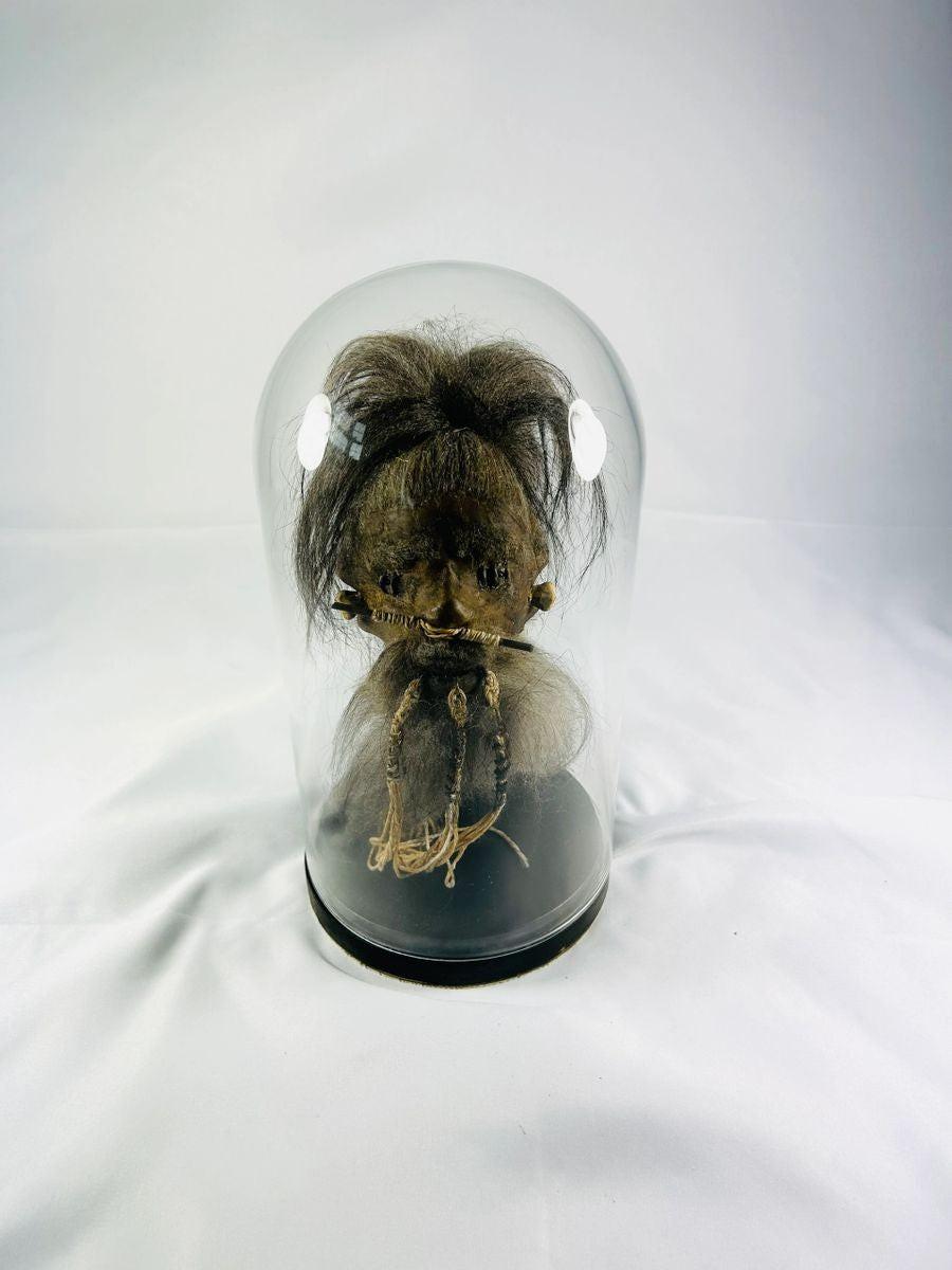 Modern replica shrunken head inspired by Jivaroan tsantsa traditions, crafted from stitched animal hide with horse hair and displayed in a glass globe
