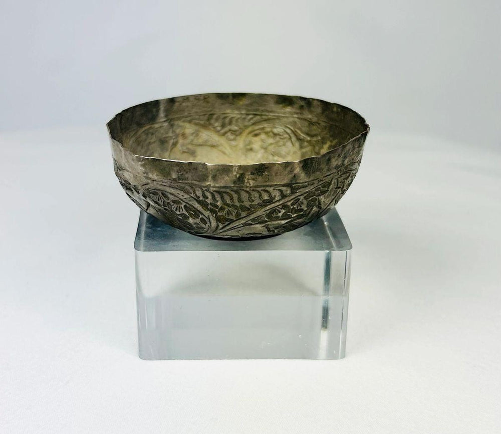 Seljuk Persian silver unguent bowl from 12th–13th century CE, featuring intricate engraved floral and geometric motifs with a natural silver patina, displayed on a clear acrylic stand under studio lighting.