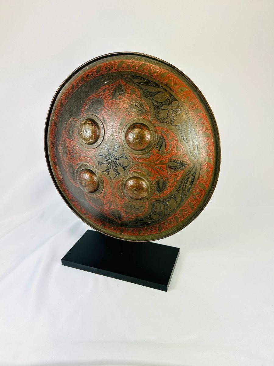 19th-century Indo-Persian warrior shield featuring intricate red and black lacquer designs and raised bosses.