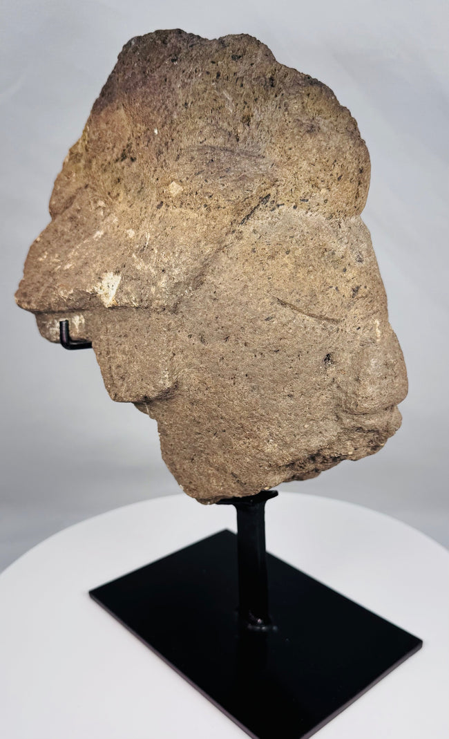 Fragmentary African carved stone head displayed on a black museum-style stand