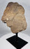 Fragmentary African carved stone head displayed on a black museum-style stand