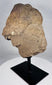 Fragmentary African carved stone head displayed on a black museum-style stand
