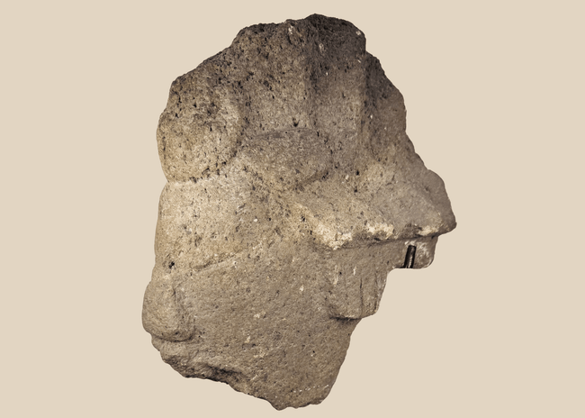 African carved stone head fragment with conical headdress on black metal display stand