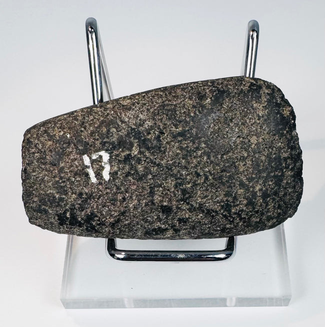 Angled view of an ancient Andean stone axe displaying its beveled edge and heavily worn archaeological surface.