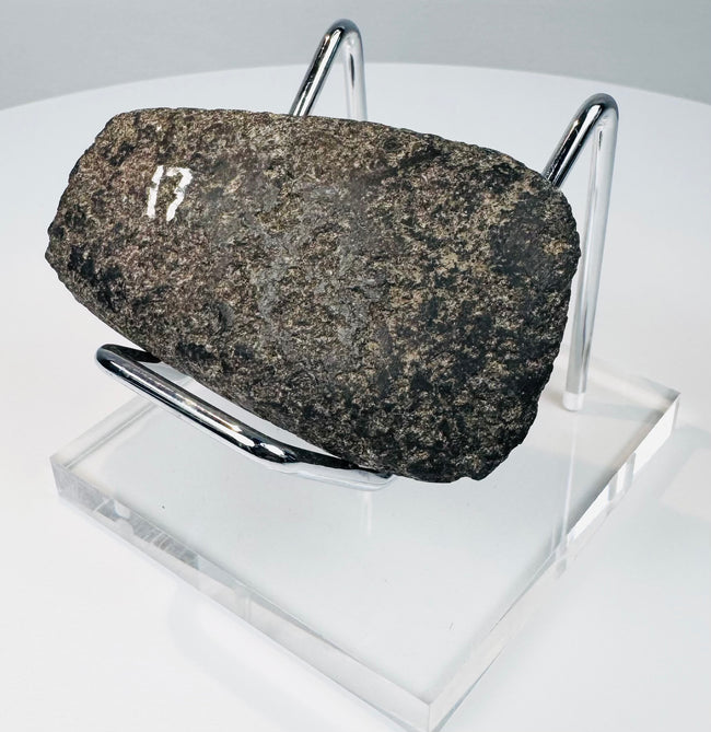 Detailed view of an ancient Ecuadorian or Peruvian ground stone axe with mottled mineral patina and surface wear.