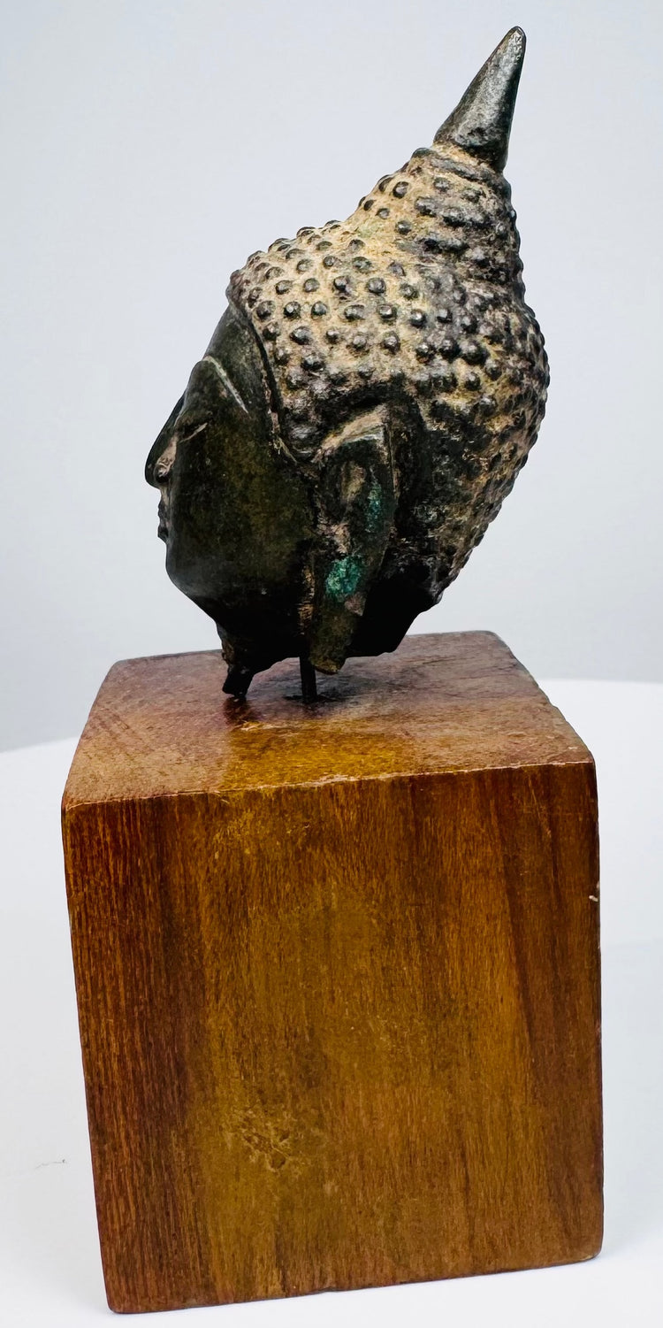 Thai bronze Buddha head with a long earlobe, curved jawline, and raised hair curls, supported above a wooden display base.