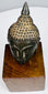 Bronze Buddha head highlighting the pointed topknot, lighter textured hair, and arched brows above half-closed eyes.