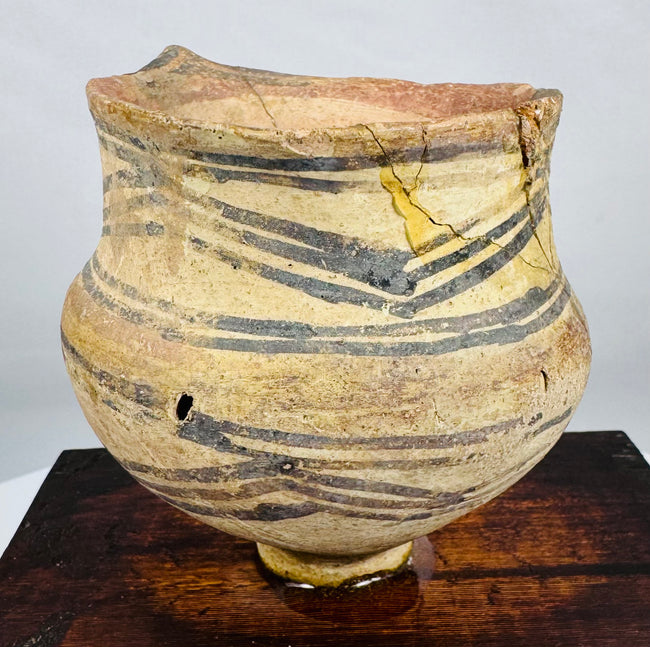 Ancient Chinese earthenware vessel displaying geometric painted motifs and mineral deposits