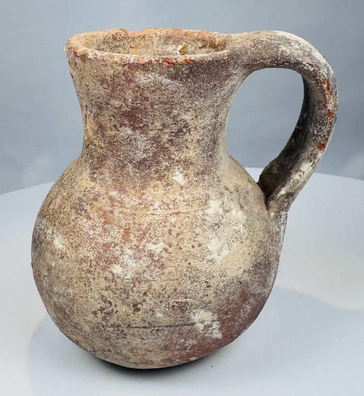 Ancient Levantine pouring vessel with rounded body and pale mineral encrustation