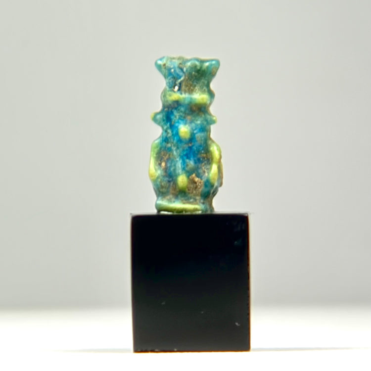 Ancient Egyptian faience amulet of deity Bes in turquoise-blue glaze on display cube
