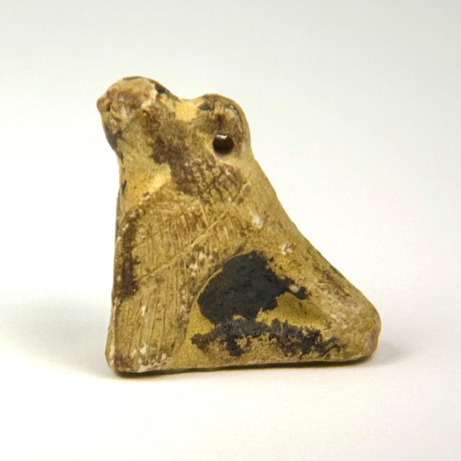 Ancient Egyptian crouching falcon pendant amulet with suspension perforation, natural patina, and worn stone surface.
