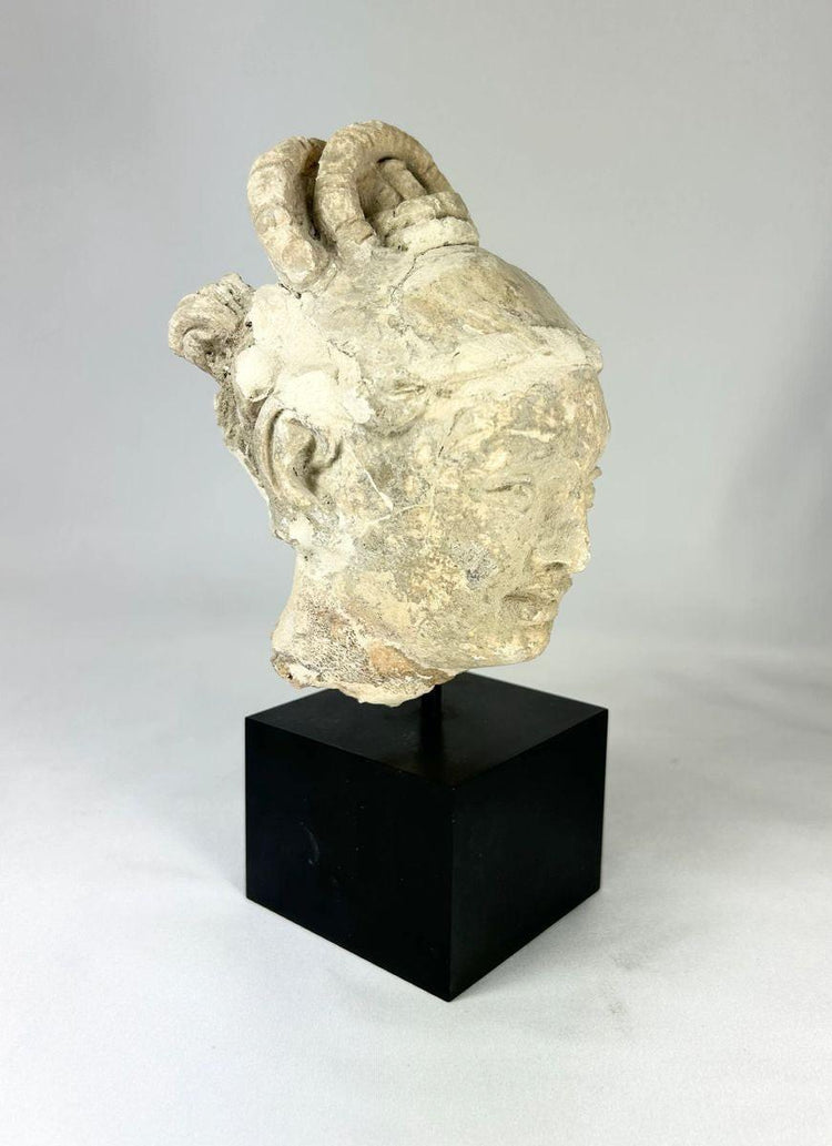 Stucco Buddha head fragment on black base, serene expression, stylized hair, partial halo, Southeast Asia, 12th–13th century CE