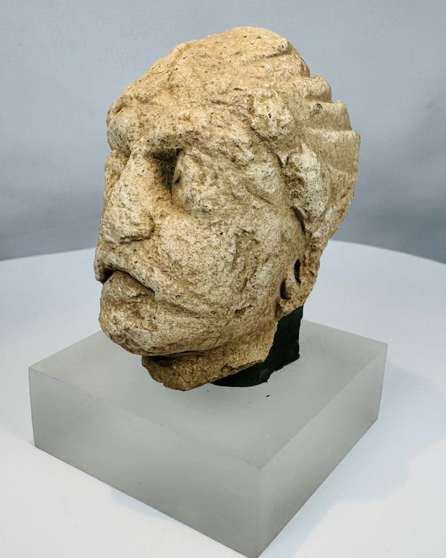 Gandharan Buddhist sculpture fragment featuring a contemplative face, wavy coiffure remnants, and centuries of weathering.